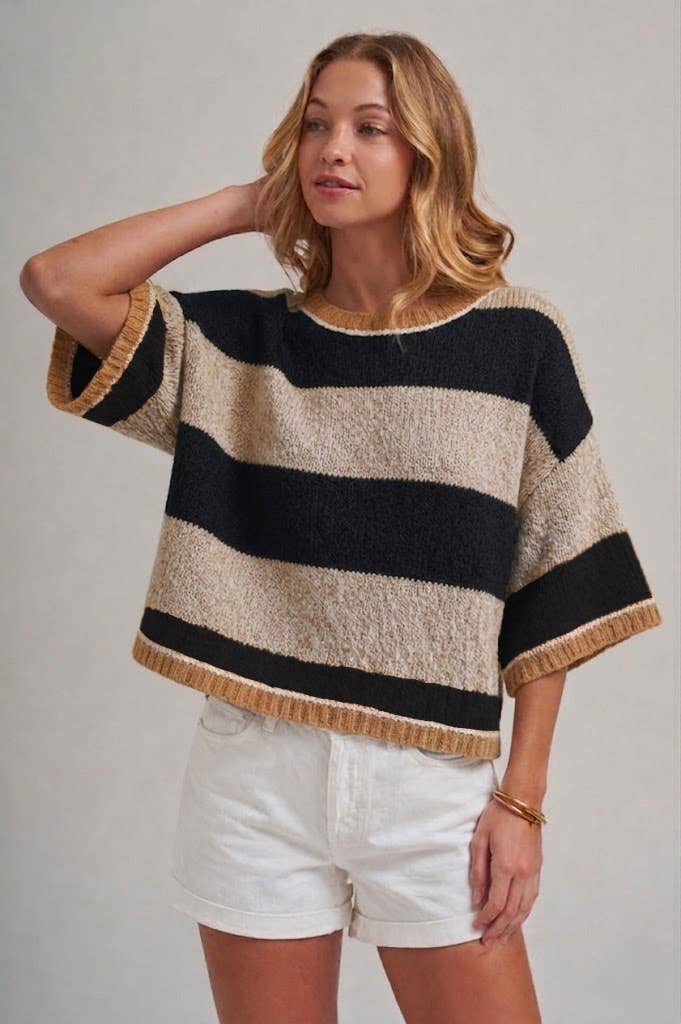 Woman wearing a black and beige striped sweater with white shorts on a plain background