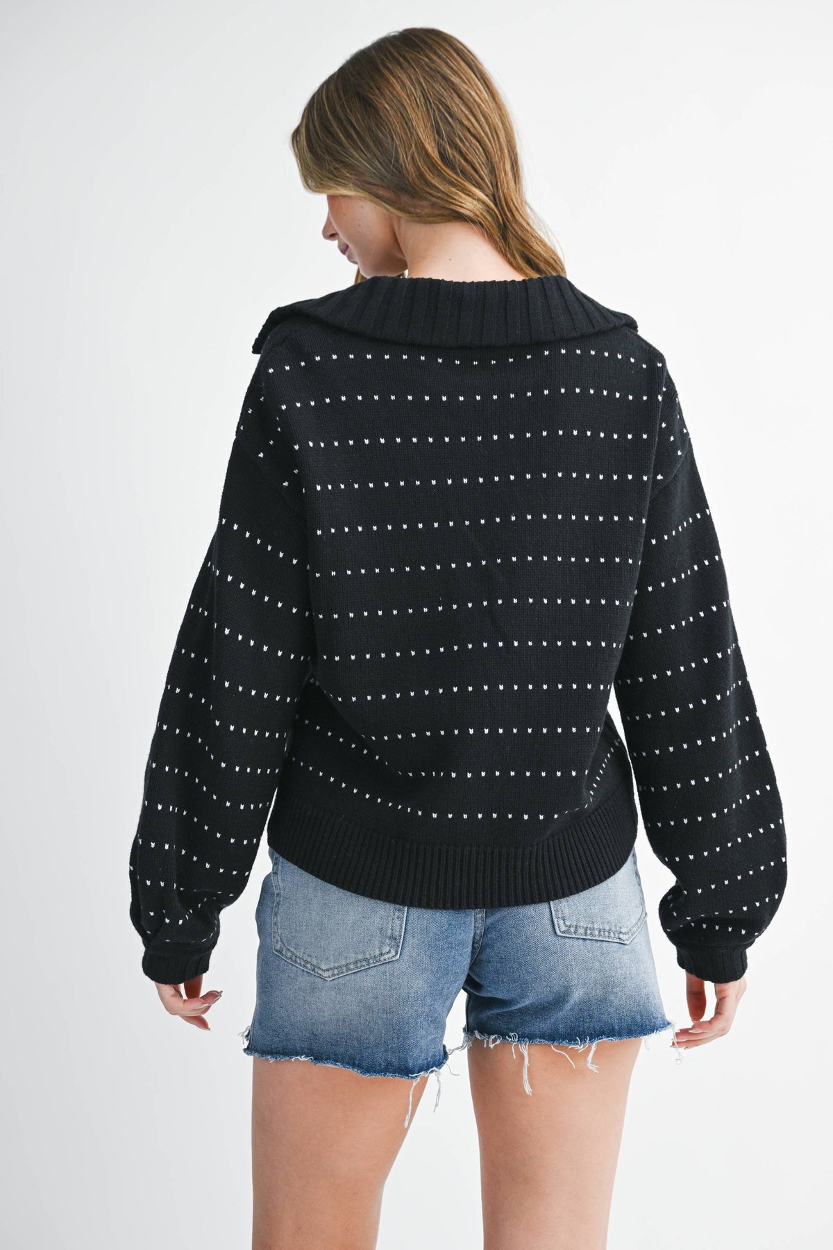 Person wearing a black patterned sweater and denim shorts on a white background
