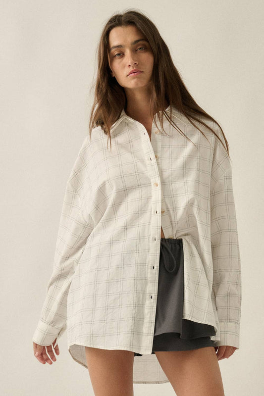 A woman modeling a long-sleeve button-front shirt in a light beige and white windowpane plaid pattern, styled over a black skirt against a plain beige studio background.