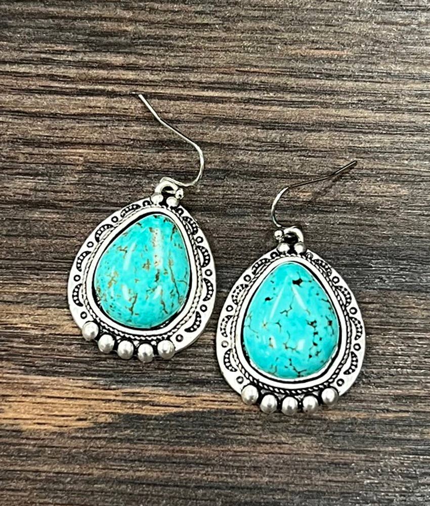 Turquoise teardrop earrings with silver detailing on a wooden surface