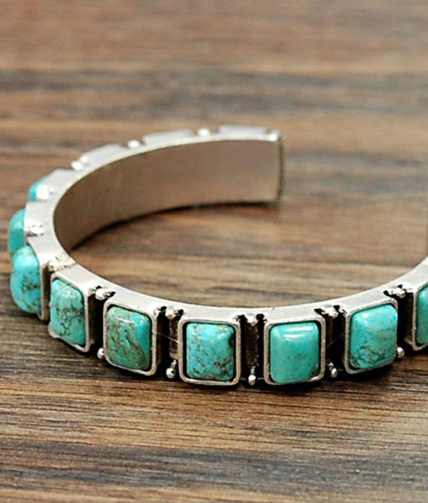 Silver cuff bracelet with turquoise stones on a wooden surface