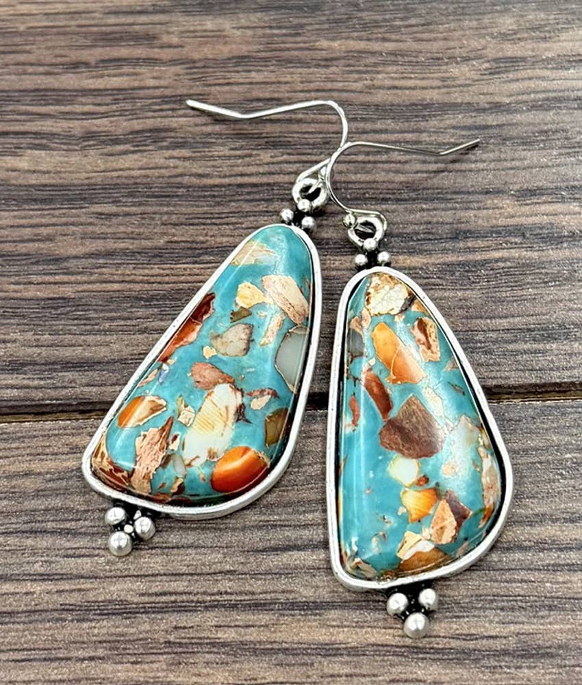A pair of silver dangle earrings with irregular turquoise-blue stone pendants containing orange, brown, and cream inclusions, displayed on a dark wood background.