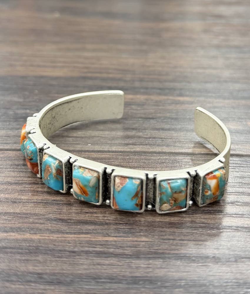 A sterling silver cuff bracelet featuring rectangular turquoise stone inlays, resting on a dark wood surface.
