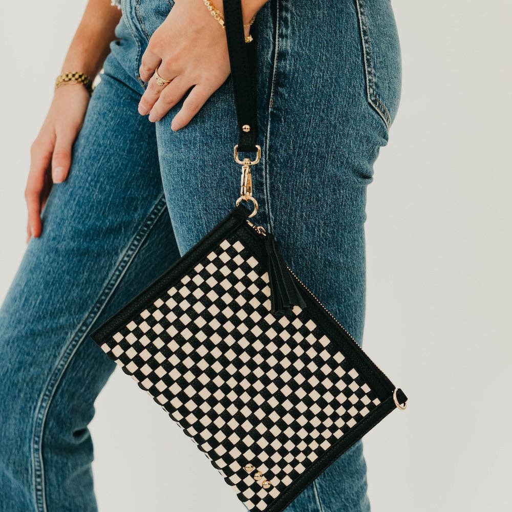 Person holding a black and white checkered clutch bag with jeans.