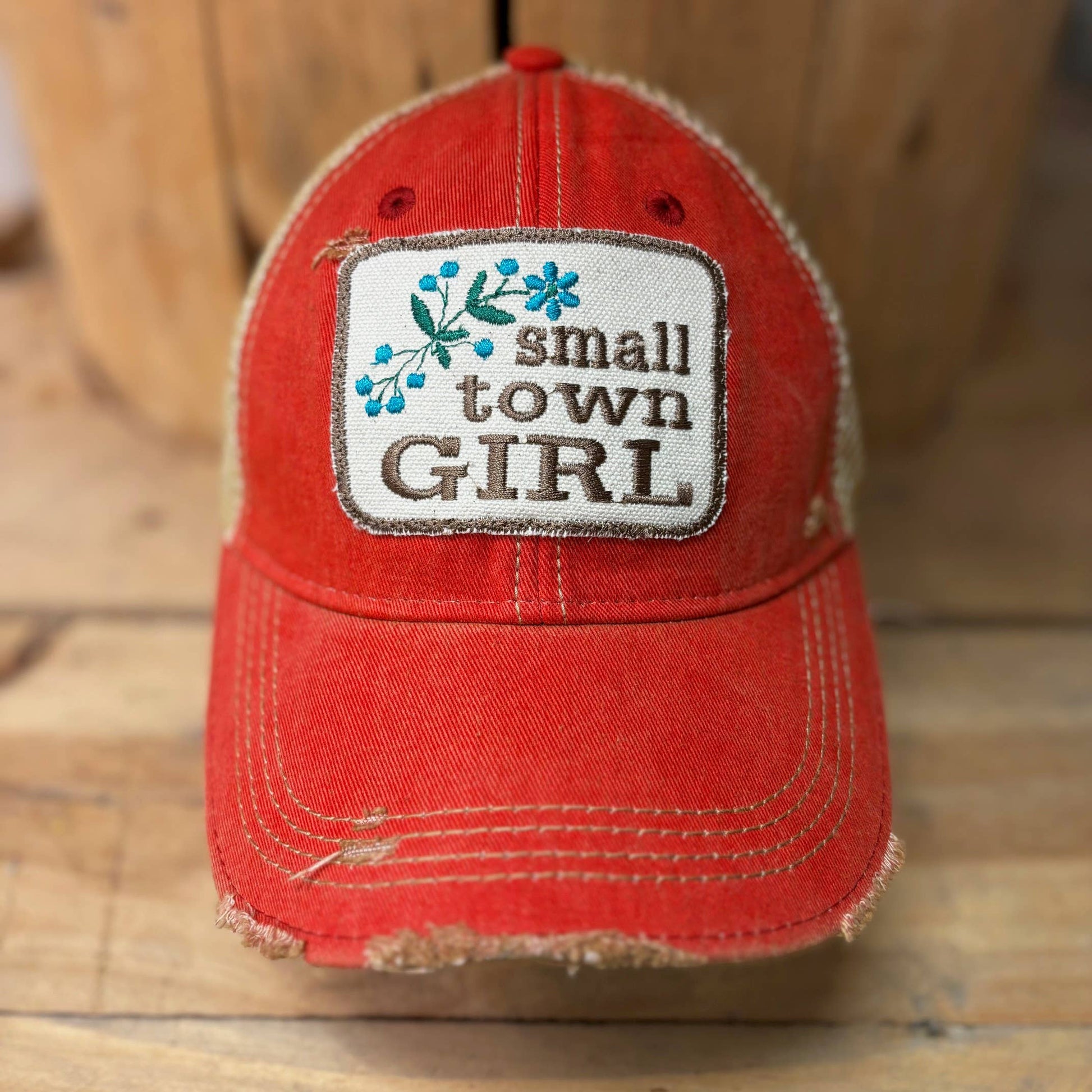 Red cap with 'small town GIRL' patch on a wooden surface