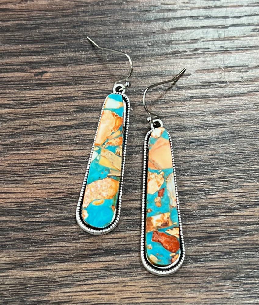 Turquoise and gold patterned earrings on a wooden surface