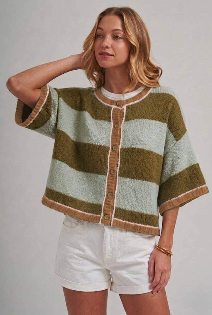 Woman wearing a green and beige striped sweater with white shorts on a plain background