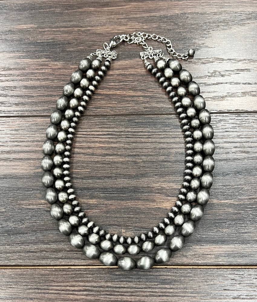 Triple strand silver beaded necklace on a wooden surface