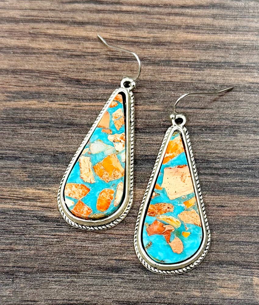 A pair of teardrop-shaped dangle earrings with turquoise and orange stone inlay and silver-toned rope border, displayed on a dark wood background.