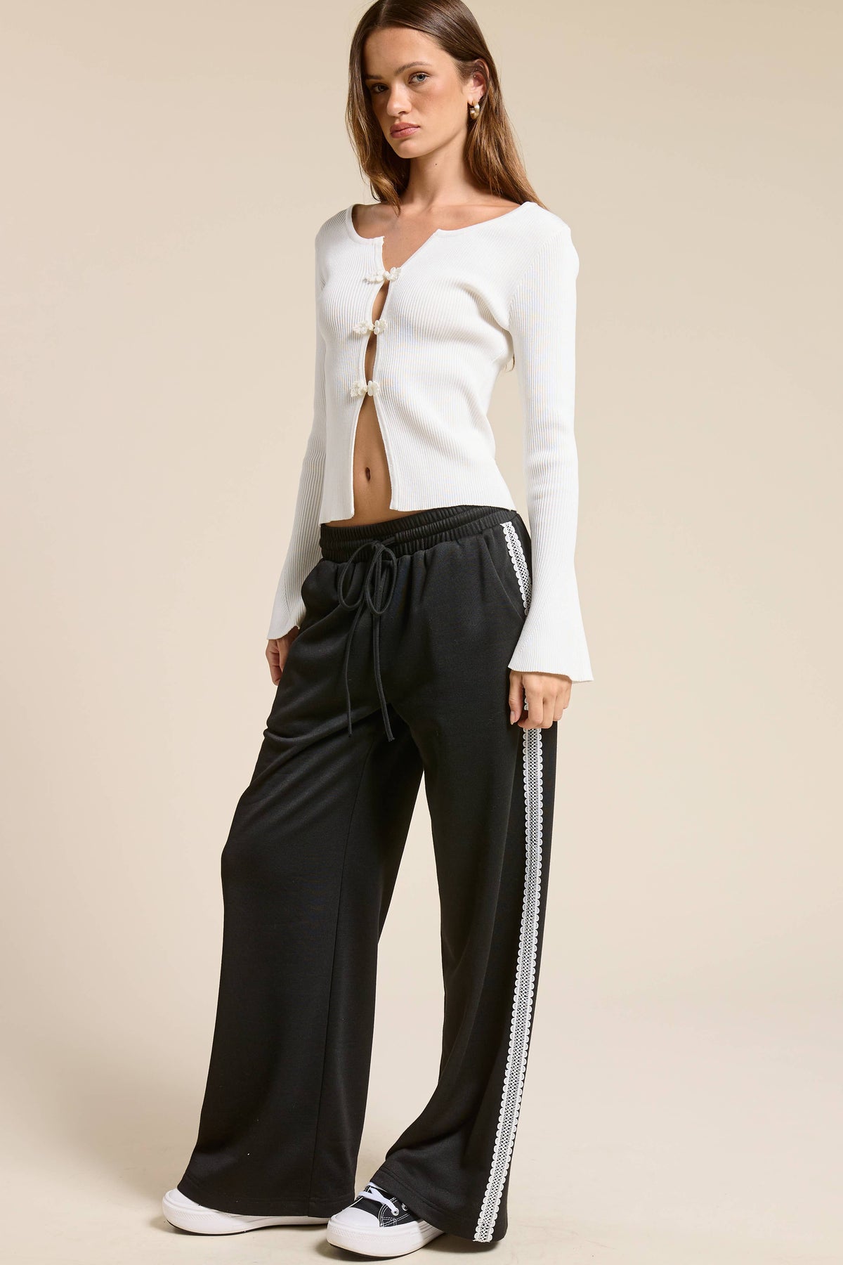 Person wearing a white long-sleeve top and black pants with a side stripe on a beige background