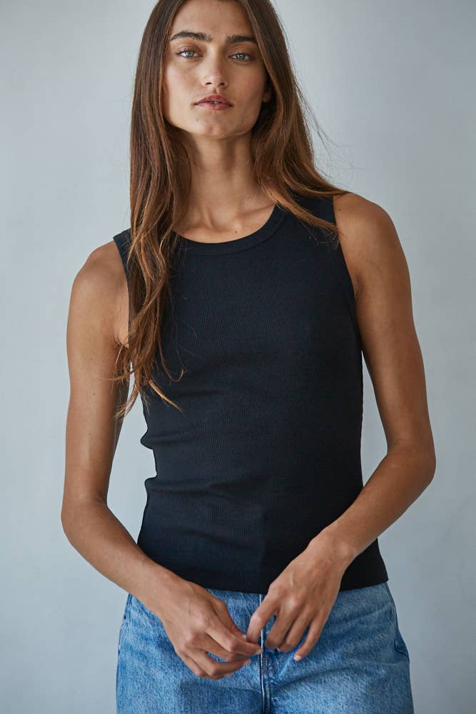 Woman wearing a black sleeveless top and blue jeans against a gray background