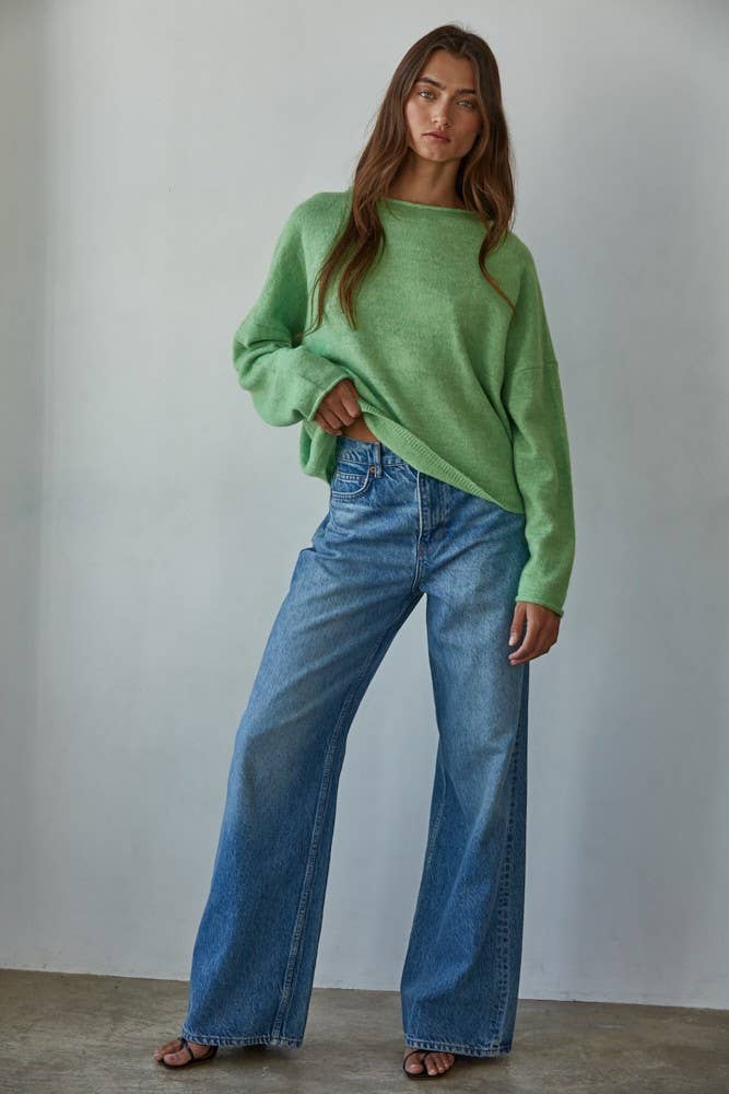 Woman wearing a green sweater and blue jeans against a plain background