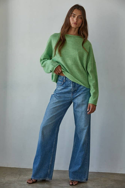 Woman wearing a green sweater and blue jeans against a plain background