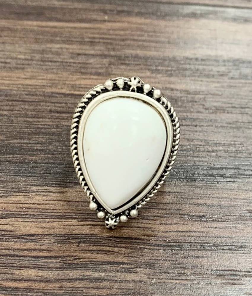 A teardrop-shaped silver ring featuring a smooth, off-white cabochon stone, set against a dark wood background.