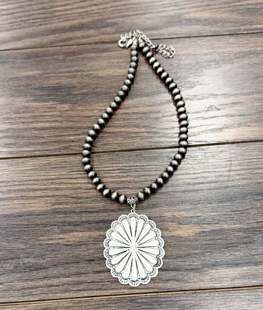 Necklace with beaded chain and silver pendant on a wooden surface