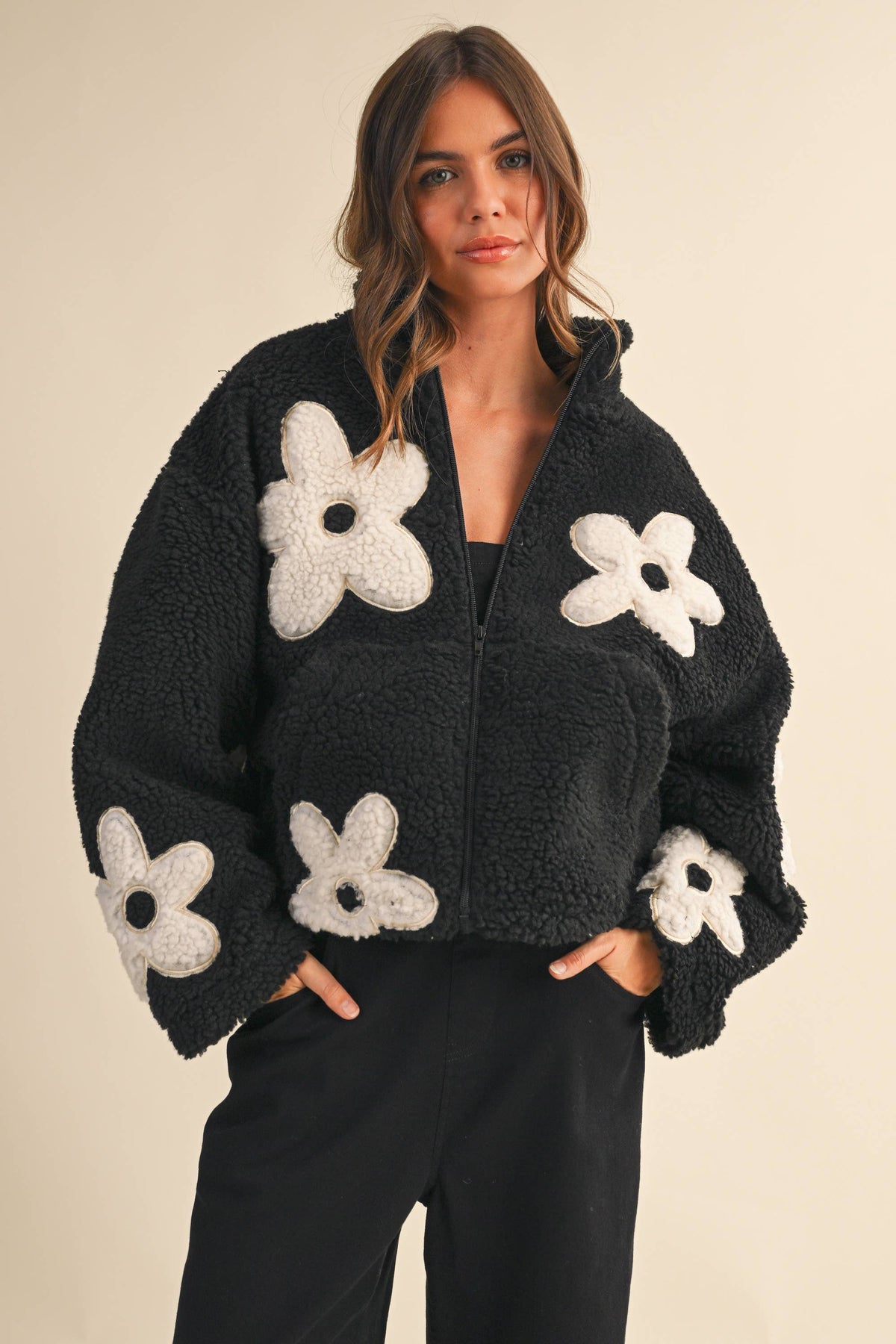 Woman wearing a black fleece jacket with white floral patterns on a beige background