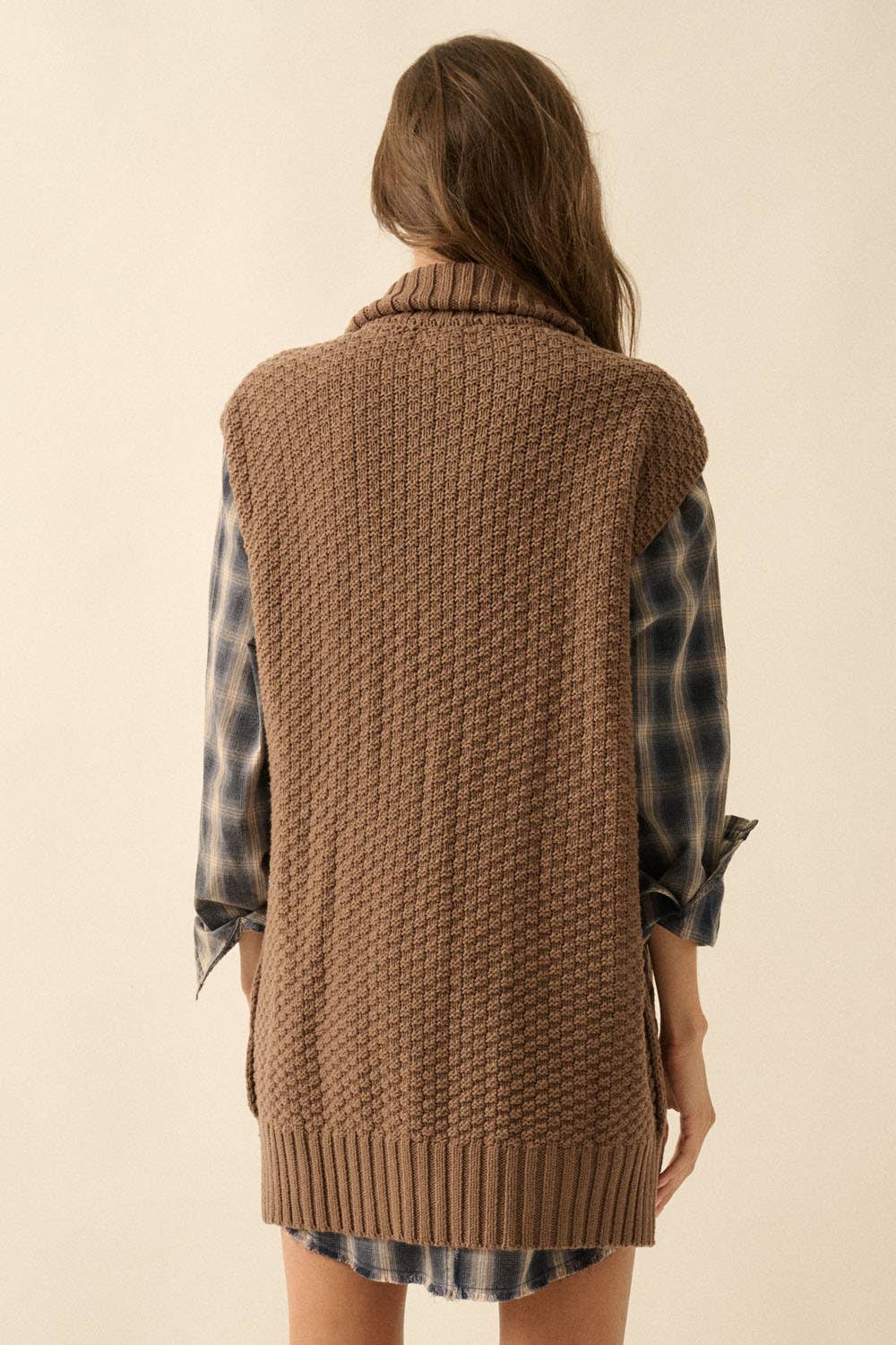 Woman wearing a brown knitted vest over a plaid shirt on a beige background