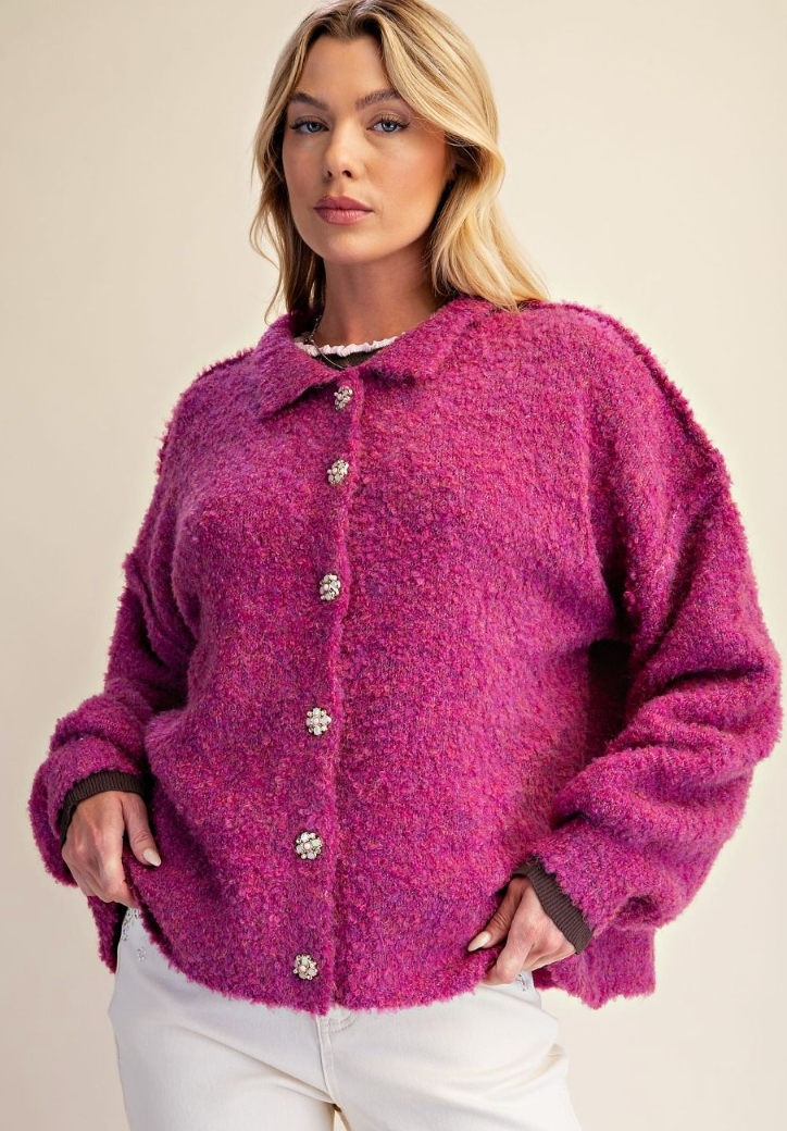A woman wearing a fuzzy, textured magenta-pink button-up cardigan with white pants, photographed against a plain beige studio background.