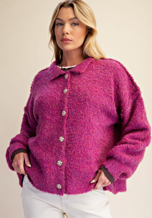 A woman wearing a fuzzy, textured magenta-pink button-up cardigan with white pants, photographed against a plain beige studio background.