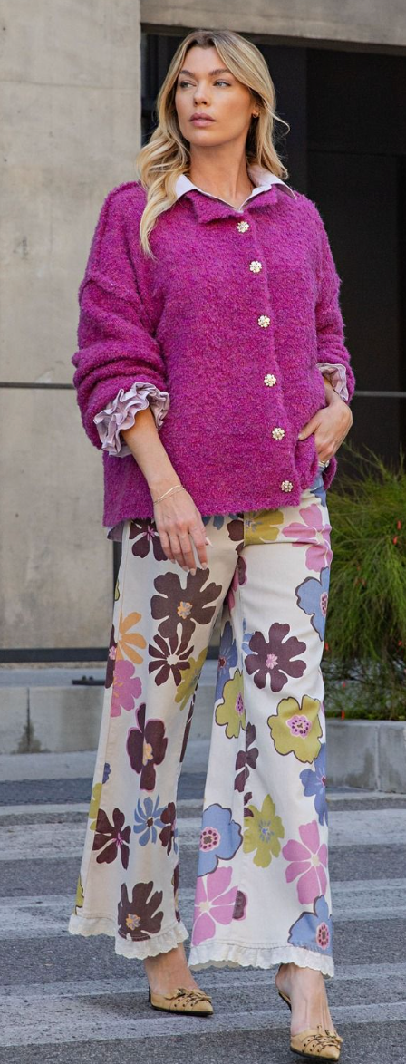 A woman modeling a vibrant magenta textured button-up cardigan and wide-leg floral print pants with leopard print flats, set against a modern concrete building background.