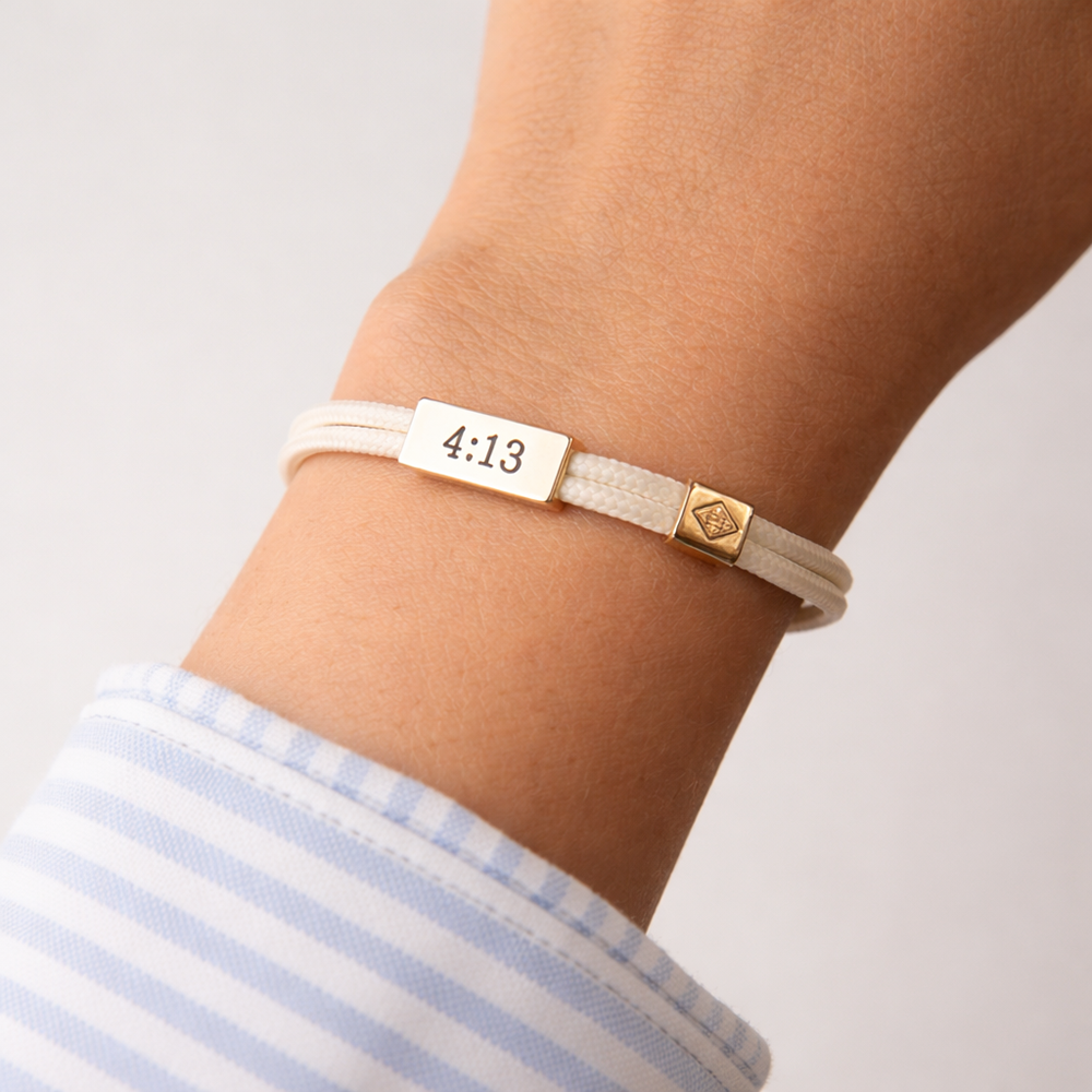 Bracelet with a gold tag displaying '4:13' on a wrist against a light background