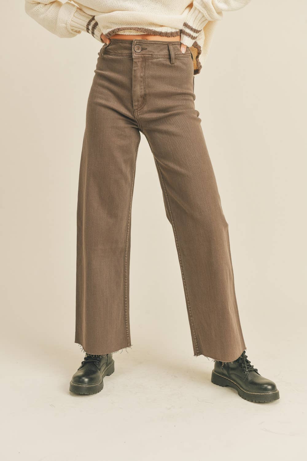 Person wearing brown wide-leg pants and black shoes on a beige background