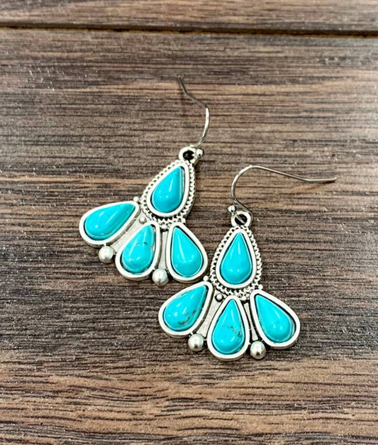 A pair of turquoise and sterling silver dangle earrings displayed on a rustic brown wooden surface.