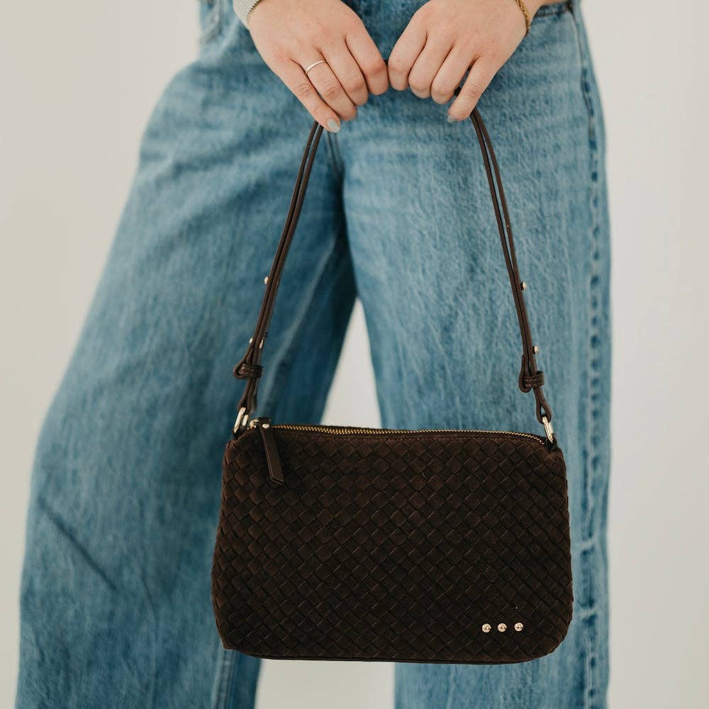 Person holding a black woven handbag with blue jeans in the background