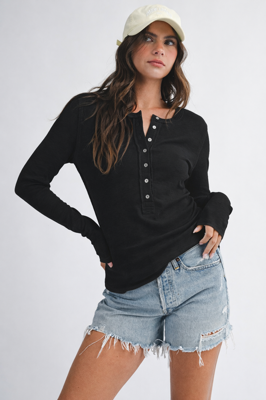 Woman wearing a black long-sleeve top and denim shorts on a white background
