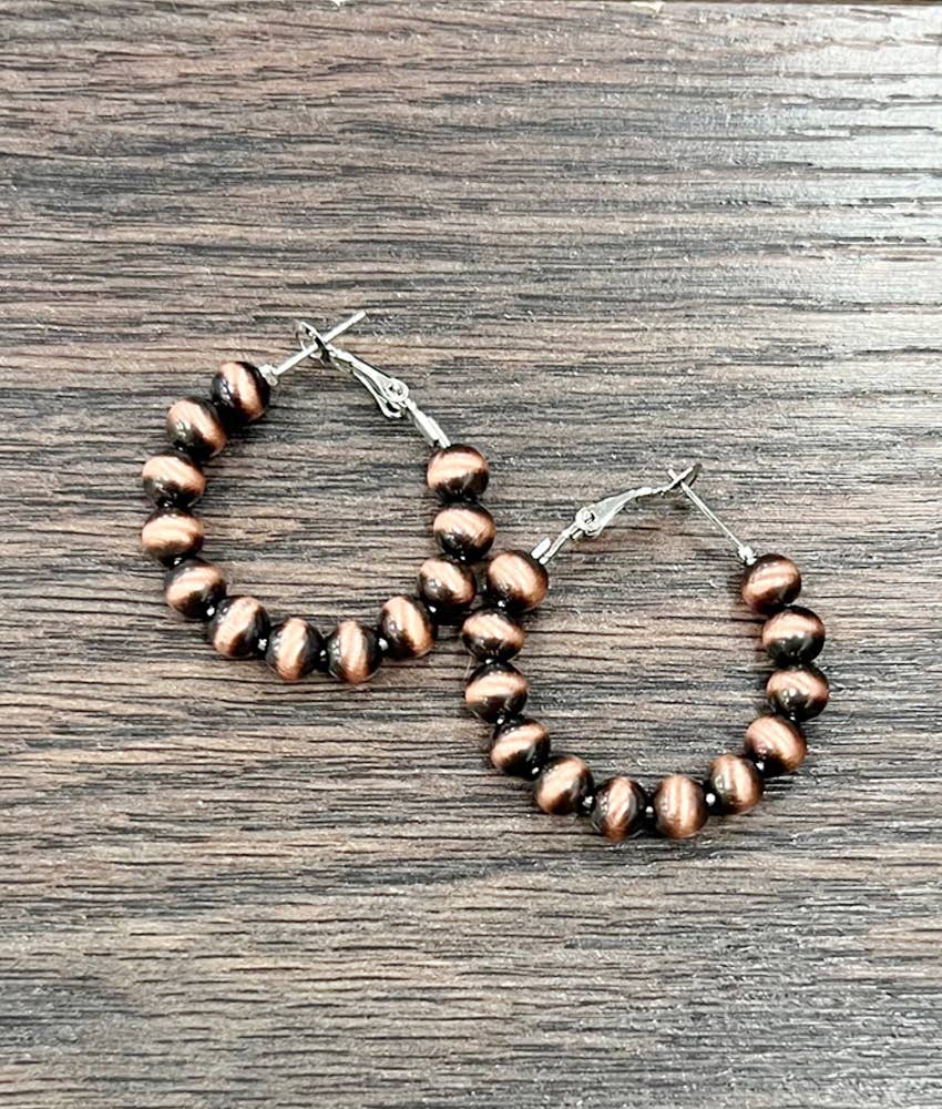Pair of copper beaded hoop earrings on a wooden surface