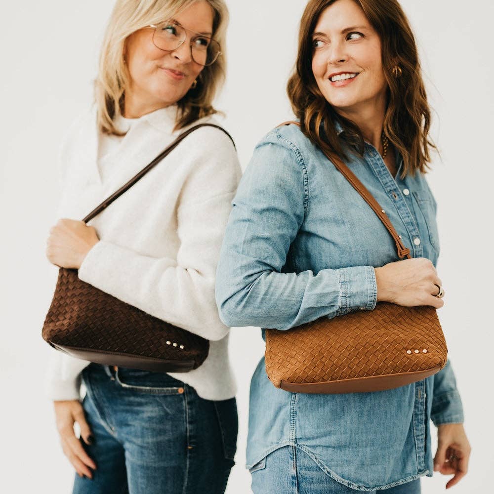 Two women holding brown handbags against a plain background