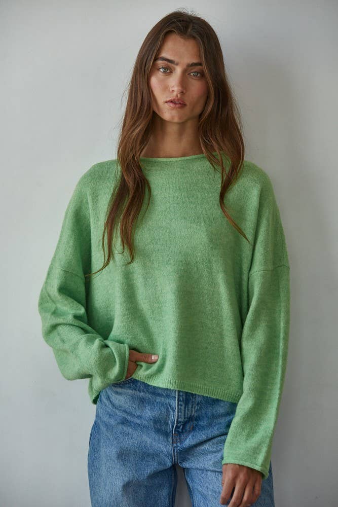 Woman wearing a green sweater and blue jeans against a plain background