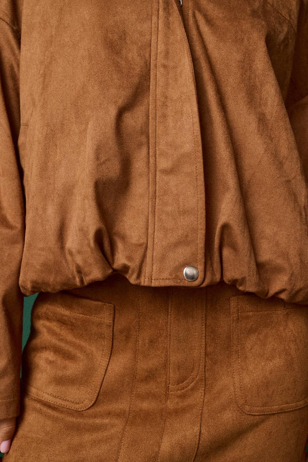 Close-up of a brown suede or faux-suede jacket or overshirt with a silver snap button, paired with matching brown bottoms.