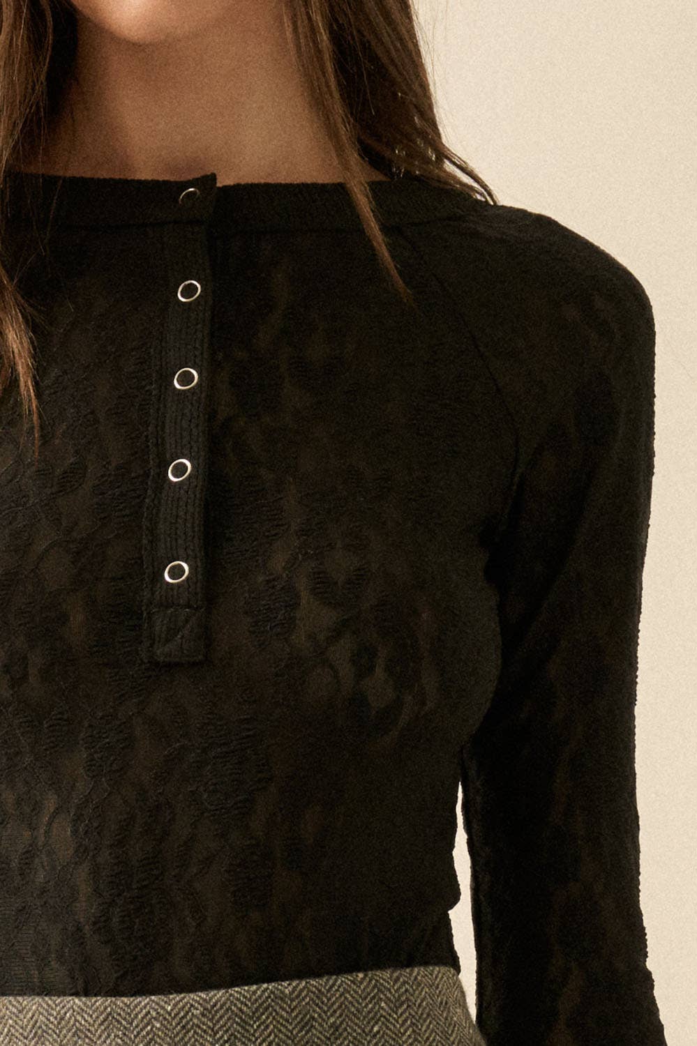 Close-up of a black lace textured long-sleeve top with silver buttons on a neutral background